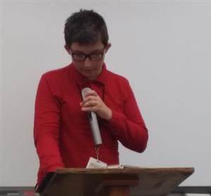 Middle school student holds a microphone while reciting a poem. 